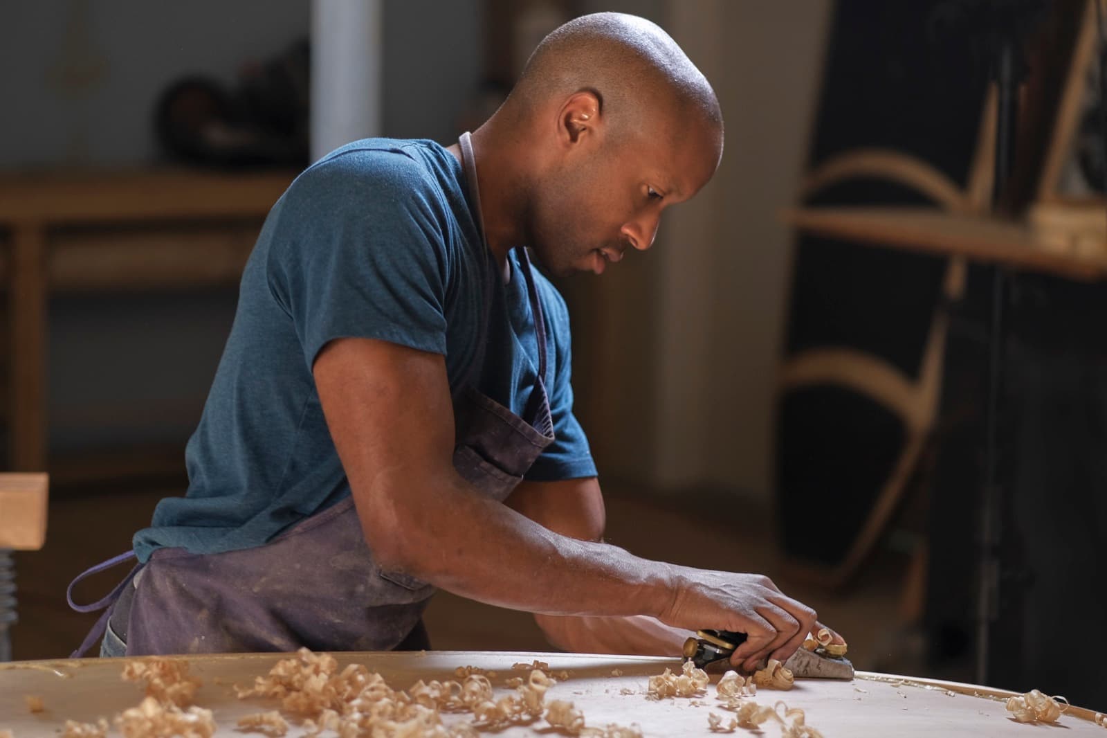 Furniture maker hand-planing a tabletop in a wood shop